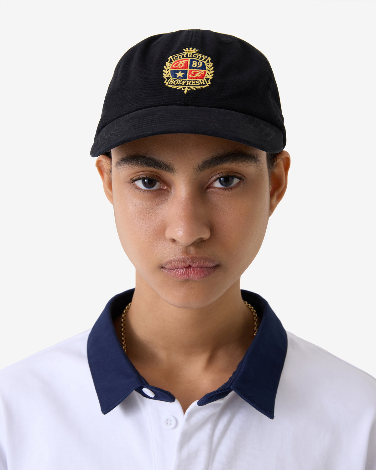 Person wearing a black cap with a logo and a white shirt with blue collar.
