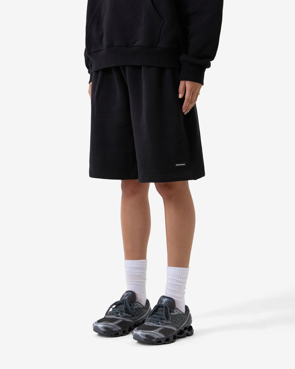 Person trägt ein schwarzes Outfit mit Shorts, schwarzen Schuhen und weißen Socken auf weißem Hintergrund