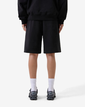 Person trägt ein schwarzes Outfit mit Shorts auf weißem Hintergrund