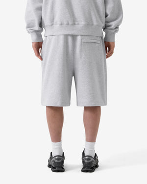 Person trägt graues Sweatshirt und Shorts mit schwarzen Schuhen auf weißem Hintergrund
