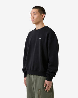 Person trägt ein schwarzes Sweatshirt mit einem kleinen Logo auf weißem Hintergrund