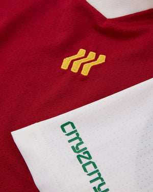 Nahaufnahme eines rot-weißen Sporttrikots mit gelbem Logo und grünem Text.