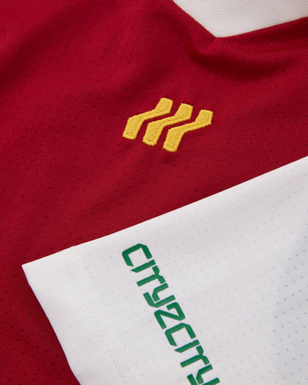 Nahaufnahme eines rot-weißen Sporttrikots mit gelbem Logo und grünem Text.