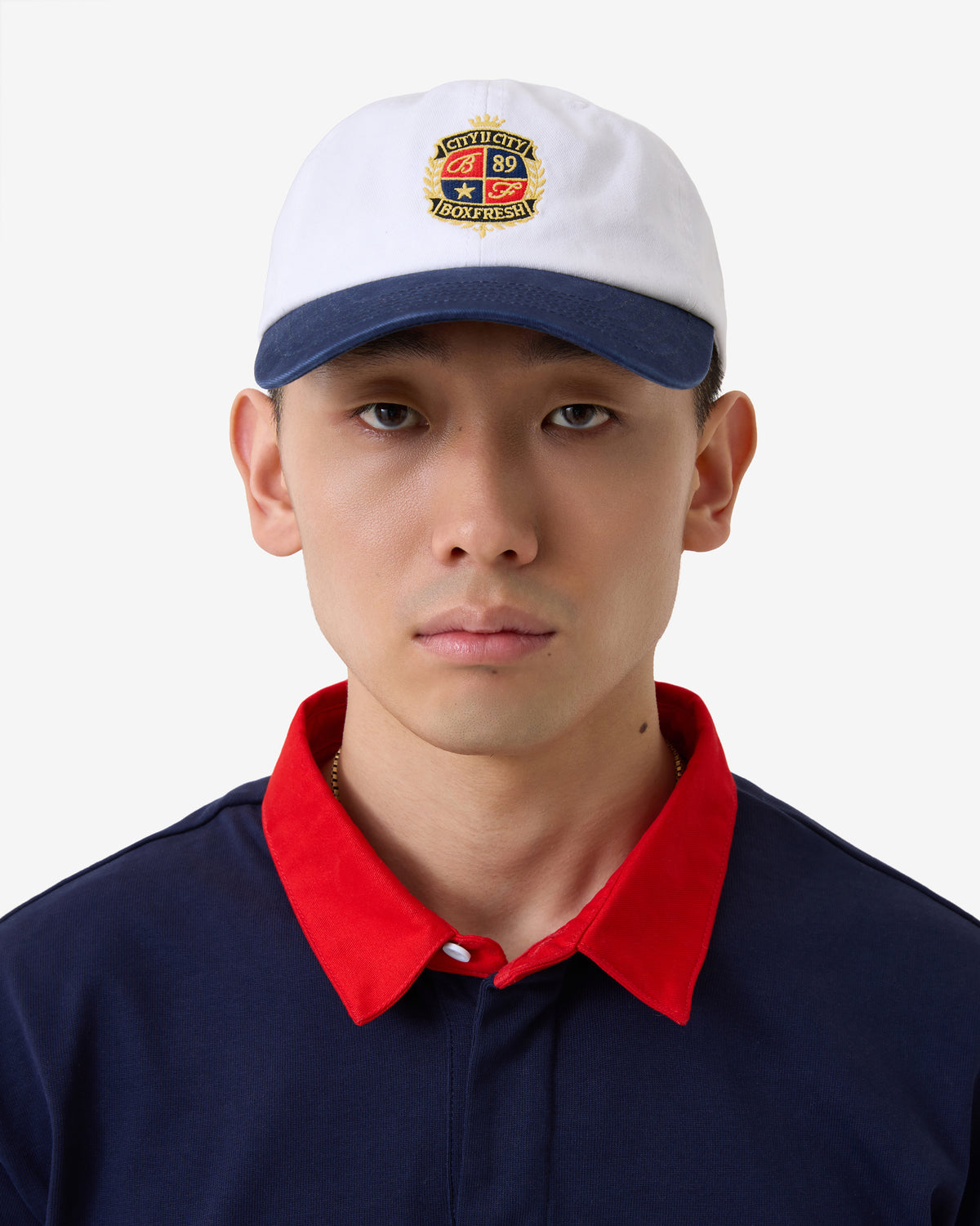 Person wearing a white cap with a logo and a navy shirt with a red collar.